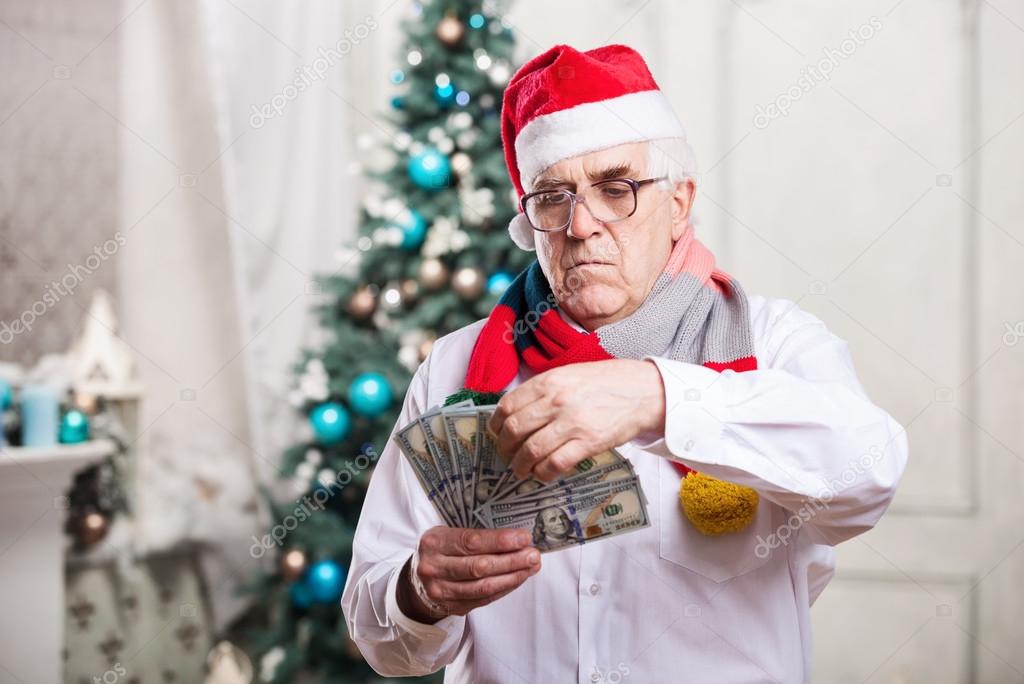 Senior man in Santa's hat holding money on Christmas background