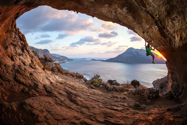 Manliga rock klättrare klättrar längs ett tak i en grotta vid solnedgången — Stockfoto