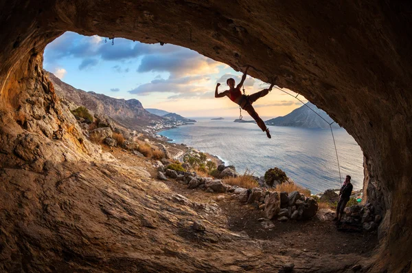 Vrouwelijke rock klimmer die zich voordeed tijdens het klimmen langs dak in grot bij zonsondergang — Stockfoto