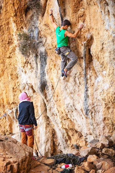 Young man lead climbing on natural cliff, belayer watching him — Stock Photo, Image