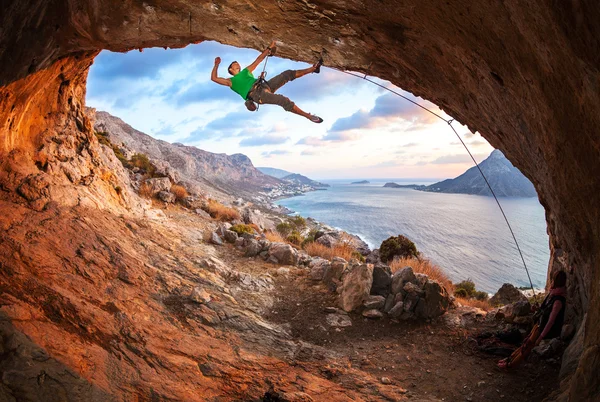 Hombre escalador escalando a lo largo de un techo en una cueva al atardecer — Foto de Stock