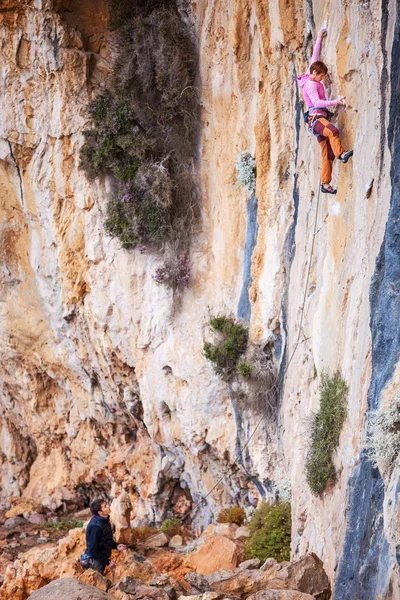 Jonge vrouw lood klimmen op natuurlijke klif, belayer kijken naar haar — Stockfoto