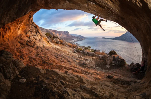 Muž horolezec stoupání podél střechy v jeskyni při západu slunce — Stock fotografie