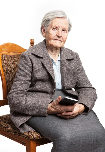 Äldre kvinna sitter på stol och hålla mobiltelefon — Stockfoto