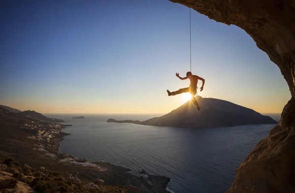 Rock klimmer opknoping op touw terwijl leiden klimmen bij zonsondergang, met Telendos island in de achtergrond — Stockfoto