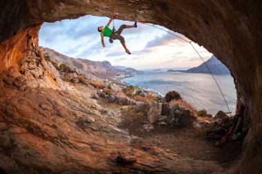 Bir mağarada bir çatı boyunca gün batımında erkek rock tırmanma. Kalymnos Island, Yunanistan