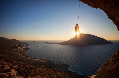 Halat kurşun gün batımında, arka planda Telendos Adası ile tırmanma sırasında asılı dağcı. Kalimnos adası, Yunanistan.