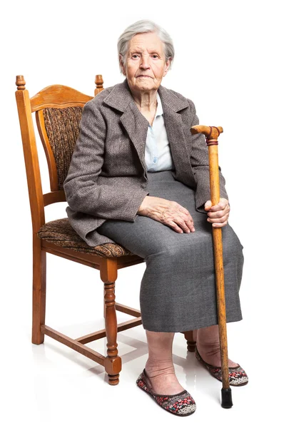 Senior woman with walking stick sitting on chair over white background — Stock Photo, Image