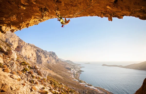 Hombre escalador escalando a lo largo de un techo en una cueva al atardecer — Foto de Stock