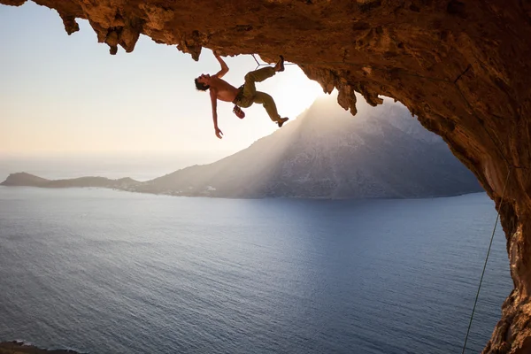 Scalatore di roccia che sale lungo il tetto in grotta al tramonto — Foto Stock