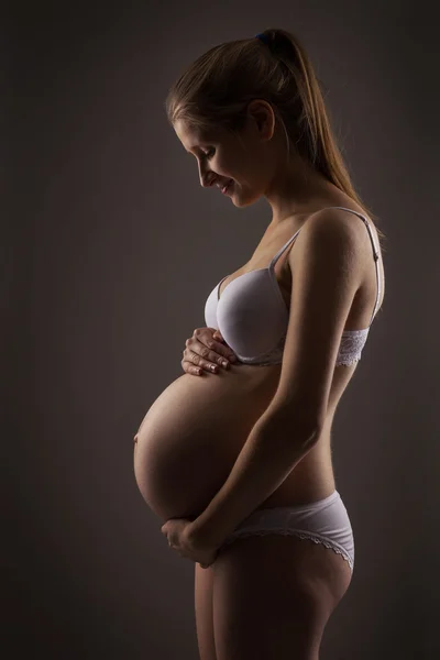 Mulher grávida sorrindo enquanto olha para a barriga — Fotografia de Stock