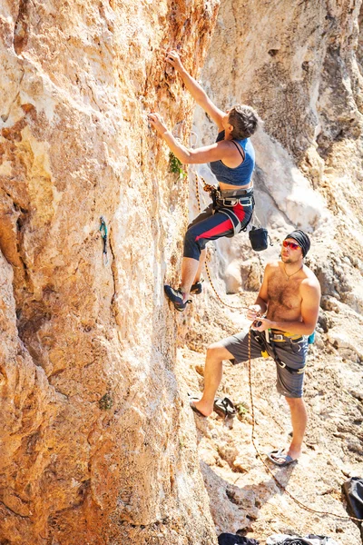 Senior vrouw lood klimmen op klif, guy belayer kijken naar haar — Stockfoto