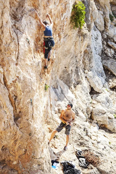 Senior vrouw leiden klimmen op natuurlijke klif, guy belayer kijken naar haar — Stockfoto