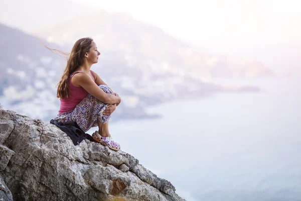 Genç bir kadın kayanın üzerinde oturuyor.