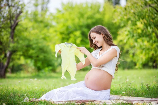 Mujer embarazada sosteniendo traje de bebé — Foto de Stock
