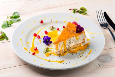 Beyaz tabakta yenilebilir çiçeklerle süslenmiş cheesecake. Beyaz ahşap bir masada bir parça cheesecake.