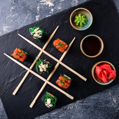 Japon suşi seti Maki siyah bir levhada TIC taktik ayak parmağı gibi sopayla yuvarlanıyor. Koyu arkaplan yaratıcı kavram suşisinde tic tac toe sushi.