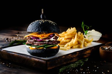 Siyah hamburgerli, patates kızartmalı, ahşap kesme tahtasının üstünde.
