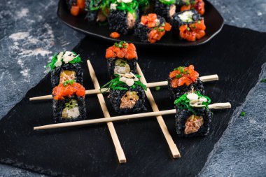 Japon suşi seti Maki siyah bir levhada TIC taktik ayak parmağı gibi sopayla yuvarlanıyor. Koyu arkaplan yaratıcı kavram suşisinde tic tac toe sushi.