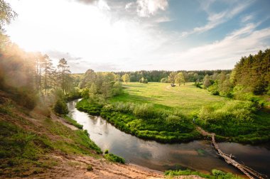 Nehir manzarası. Yüksek sarp bir bankadan güzel bir nehir manzarası, otlarla kaplanmış. Nehrin güzel güneşli manzarası yüksek kıyıları, mavi gökyüzü ve yazın yeşil otları
