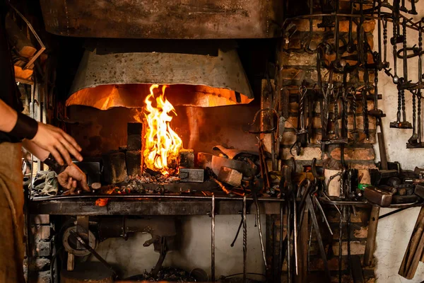 blacksmith holds billet over hot coals in clay oven. blacksmith heating iron metal sword manufacturing marching forge, Hands of blacksmith holding steel in fire of a red-hot forge