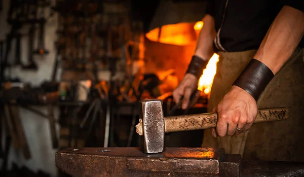 blacksmith performs forging of hot glowing metal on anvil, blacksmith manually forging molten metal on anvil in smithy workshop panorama with copy space