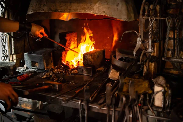 Schmied hält Knüppel über heiße Kohlen im Lehmofen. Schmied heizt eisernes Metallschwert bei der Herstellung von Marschschmieden, Schmiedehände halten Stahl im Feuer einer glühenden Schmiede — Stockfoto