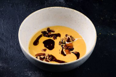 Balkabağı kremalı siyah seramik kase. Balzamik soslu. Arka planda balkabağı çorbası.