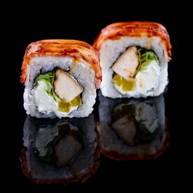 Asya mutfağı kavramı. Japon menü kafesi, restoranı ve suşi barı için siyah arka planda farklı doldurulmuş iki rulo suşi. Yansıması olan iki suşi rulosu.