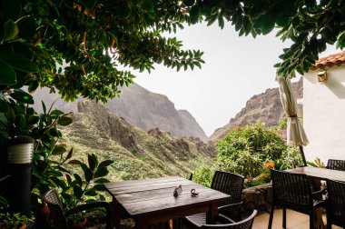 Yeşil korkulukların arkasındaki açık havada, boş bir restoranın görüntüsü. Açık hava restoranı boş masalar ve dağ manzaralı sandalyeler, güneşli bir manzara.