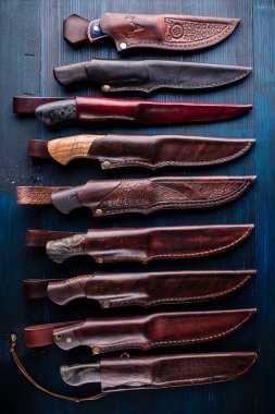 Bir sürü el yapımı bıçak, masadaki kınalı üst görüşlü av bıçakları.