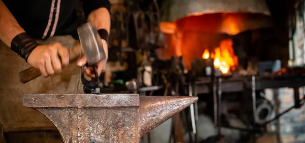 The blacksmith forging molten metal on anvil in smithy. Blacksmith at the workshop. Working metal with hammer and tools in forge