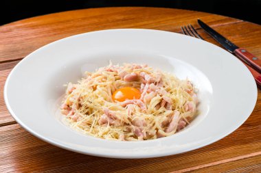 Beyaz tabakta makarna, parmesanlı ve sarısı koyu arkaplanda, peynirli makarna ve yumurta sarısı ile jambon.