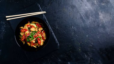 Udon siyah arka planda tavuk ve sebzeli ramen kızartır. Tavuklu hot wok, yemek çubuğu ve sosla birlikte bir tabağın üzerinde pişiyor.