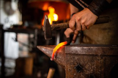 Demirci erimiş metali idare ediyor, beyaz demirci ocakta açık ateşle çalışıyor. Demirci atölyede kızgın demir dövüyor.