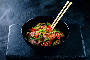 Koyu taşlı arka planda ton balıklı ve sebzeli erişte, geleneksel Asya yemekleri ton balıklı erişte, erişte kızartması ya da siyah kasede tavada erişte.