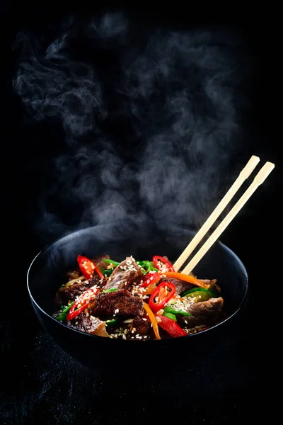 Stir fry soba noodles with beef and vegetables in wok on dark background, Asian udon noodles with beef WOK in black bowl on Slate background. Copy space