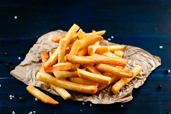 Fast food french fries potatoes served with salt and herbs on baking paper. serving of french fries on kraft paper