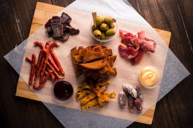 Tahta tepside mezeler, sosis, et cipsi, kızarmış ekmek ve peynir, çeşitli bira aperatifleri, kurutulmuş et, füme peynir ve ahşap arka planda sosis. Oktoberfest için bira karışık tabağı