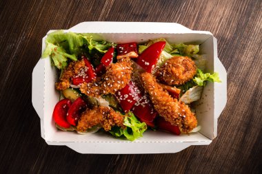 Kâğıt üzerinde kızarmış tavuk eti ile taze sezar salatası ahşap masada konteynır, tavuklu salata ve paket yiyecek teslimatında taze sebze.