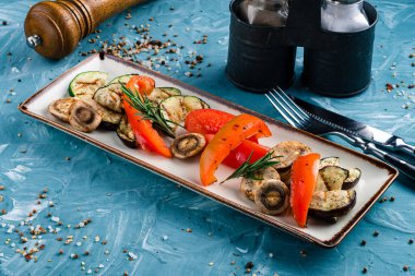 Tabağa farklı ızgara sebzeler koyun. Vejetaryen barbekü piknik seti, sıcak sebze salatası. Tabakta ızgara sıcak sebze, kabak, biber ve mantar.