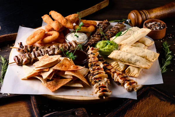 Tavuk kebabı, şiş kebap ve abur cubur soğan halkaları ve ahşap tabakta atıştırmalıklar.