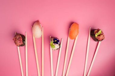 Suşi pembe arka planda tabakta. Sevgililer Günü yemeği konsepti. Metin için boşluk, pembe minimalist arka planda çubuklu düz katlı suşi ruloları