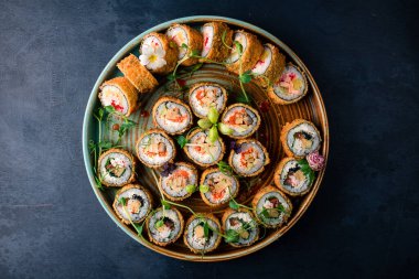 Sıcak suşi rulolarını yuvarlak tepside kızart. Lezzetli tempura ve somon, yılan balığı, salatalık, avokado, omlet ve karides karışımı. Japon Doğu mutfağı.
