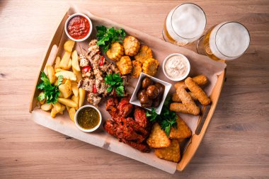 Büyük bir bira tabağı, büyük bir paket abur cubur. Karışık abur cuburlar, bol yağda kızartılmış bira. Büyük bir şirket için tatil için yiyecek. Bira için sıcak et aperatifleri ahşap tabakta servis edilir. Üst manzara, düz yatış.