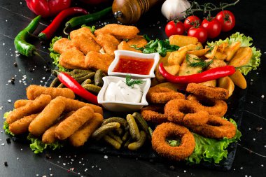 Büyük boy patates kızartması, tavuk nugget, soğan halkaları, peynir çubukları ve soslu patates kroketi. Fast Food. Karanlık arka planda tuzlu atıştırmalıklar. Gıda Konsepti Partileri