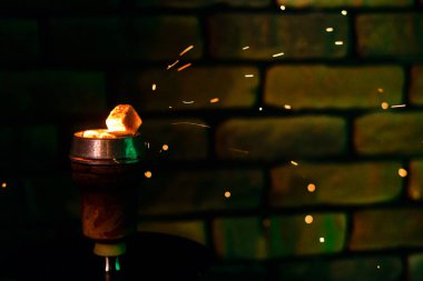 Nargile kasesindeki sıcak kömür geleneksel Asya bayramı ve sigara içmek için uçan kırmızı kıvılcımlarla ısıtılır. Karanlık bir barda nargileden kıvılcımlar saçıyor.