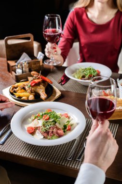 Genç çift restoranda bir kadeh kırmızı şarabı paylaşıyor, kutlama yapıyor ya da romantik bir buluşmada. Aşıklar restoranda şarap içer.