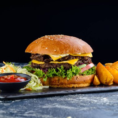Taze ev yapımı hamburger, ızgara patates ve ketçap sosuyla servis ediliyor. Koyu kırsal tarzda. Amerikan fast food konsepti. İki biftekli sulu Amerikan burgeri.