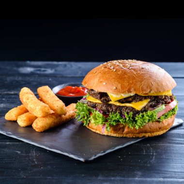 Sulu pirzolalı hamburgerler, taze sebzeler, tahtadan bir masada susam tohumlu çıtır çörekler. Geleneksel fast food. Gurme burger. Ev yapımı yemek konsepti. Koyu renk..